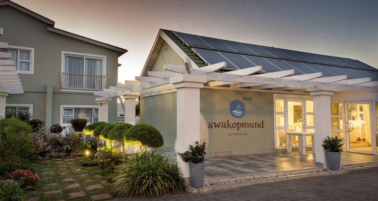 Moderner Guesthaus-Eingang mit Solarpanelen und gepflegtem Garten in der Dämmerung in Swakopmund.