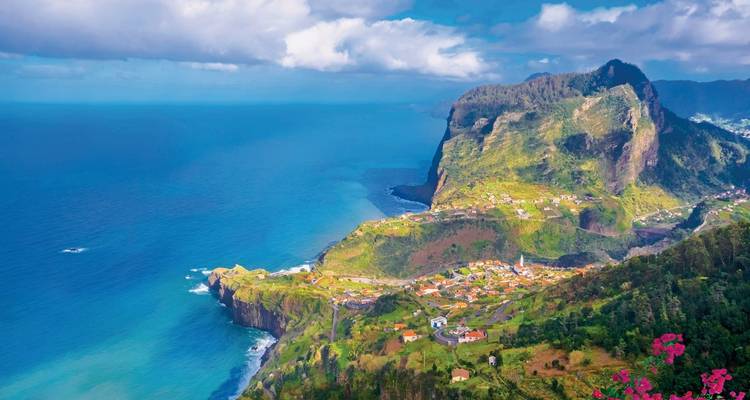Üppig grüne Klippen stürzen entlang der rauen Nordküste Madeiras unter einem fleckigen Himmel in den tiefblauen Atlantik ab.