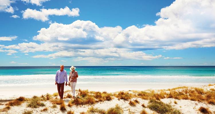 Paar spaziert an einem Strand mit klarem blauen Himmel.