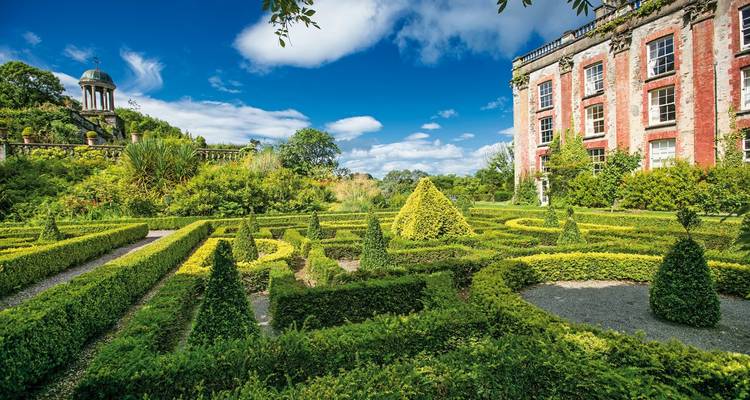 Vibrant garden with manicured hedges and an elegant building in the background.