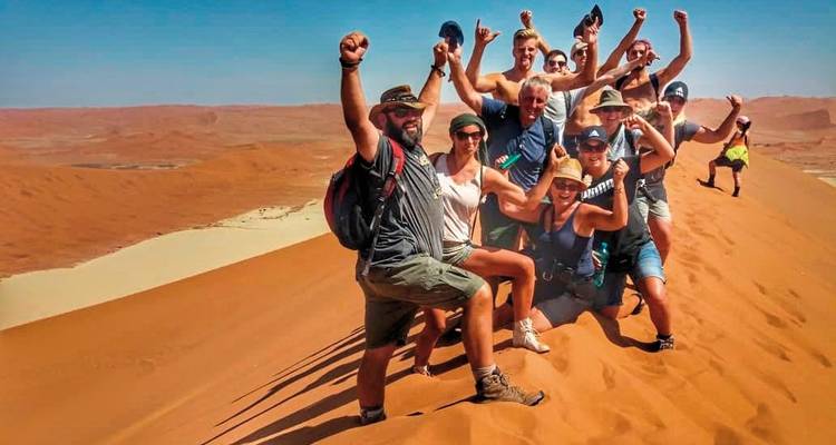 Group posing on a sand dune with arms raised.