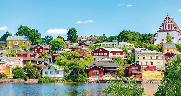 Colorful town buildings along a river with lush trees.