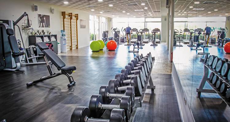 Fitness-Studio mit verschiedenen Trainingsgeräten und Spiegeln.