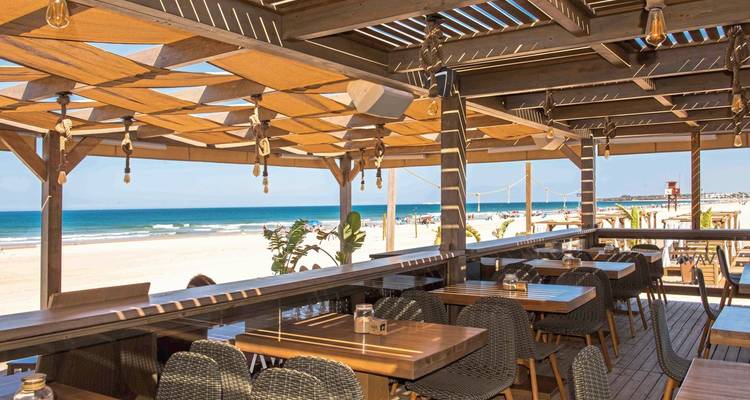 Strandrestaurant mit Holztischen und Meerblick.