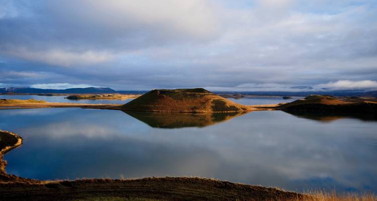 Ein ruhiger See, der den Himmel widerspiegelt, mit Hügeln im Hintergrund.