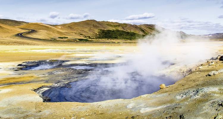 Eine dampfende geothermische Thermalquelle in einer rauen, farbenprächtigen Landschaft.