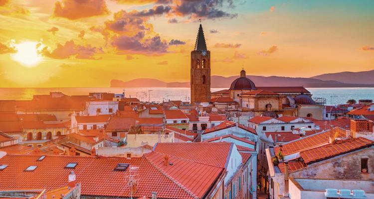 Sunset view over a town with red rooftops and a church tower.