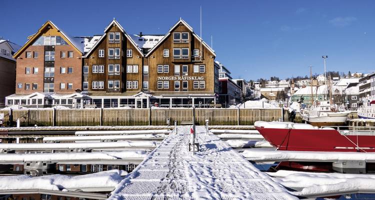Verschneiter Steg mit Gebäuden unter einem klaren blauen Himmel.