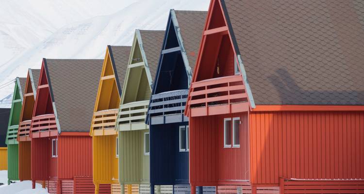 Bunte Häuser in einer Reihe unter schneebedeckten Bergen.