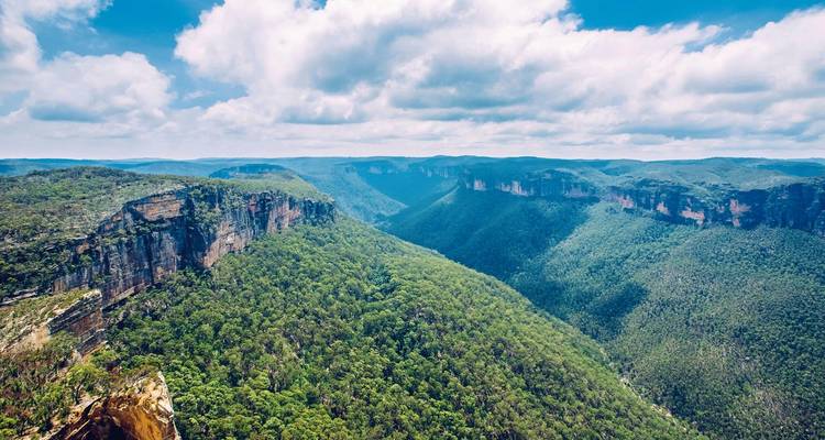 Vue large de la vallée avec des falaises verdoyantes et un ciel lumineux.