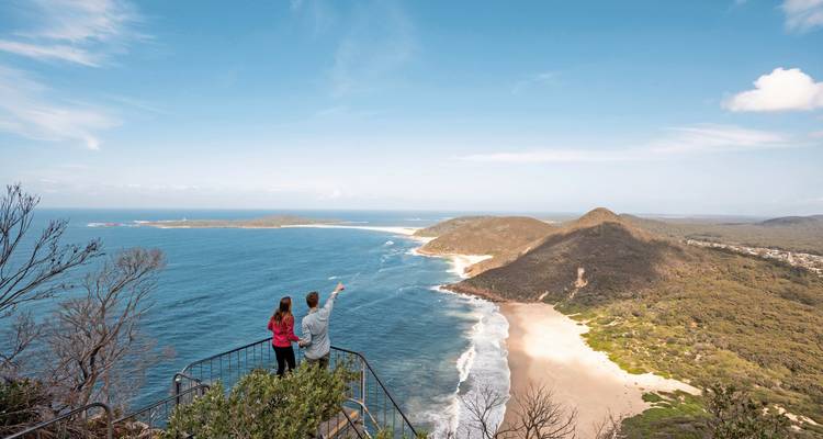 Couple debout sur un point de vue observant une vaste plage et l'océan.