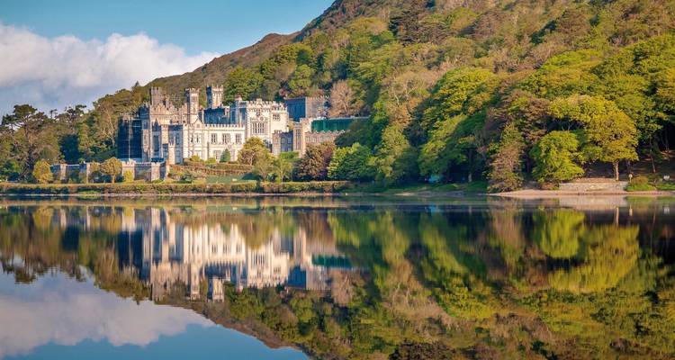 Elegant Gothic-style castle reflected perfectly in a still lake framed by lush Irish woodland
