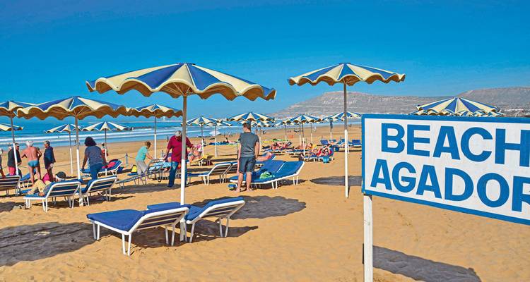 Strandszene mit Sonnenschirmen und einem Schild für Strand Agadir.