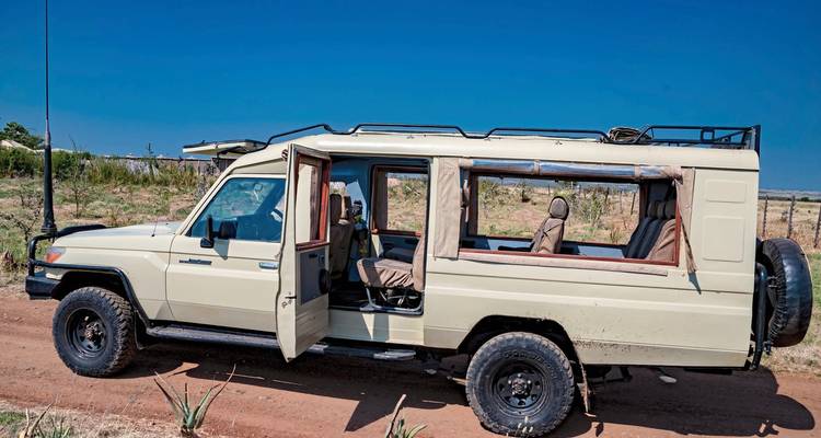 Véhicule de safari ouvert sur une route de terre dans un paysage de savane.