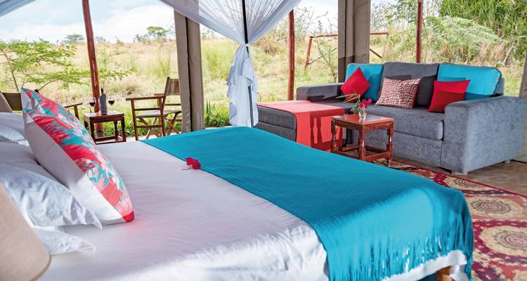 Intérieur de tente luxueux avec un lit et un coin salon, donnant sur un paysage.