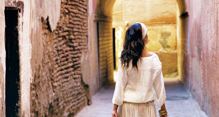 Een vrouw in traditionele kledij loopt door een smalle gewelfde steeg.