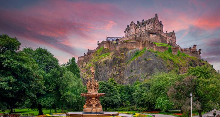 Blick auf Edinburgh Castle mit einem Brunnen im Vordergrund bei Sonnenuntergang.