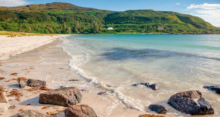 Beautiful sandy beach with clear water and a hilly green landscape.