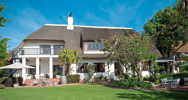 White house with a thatched roof surrounded by trees and a garden.