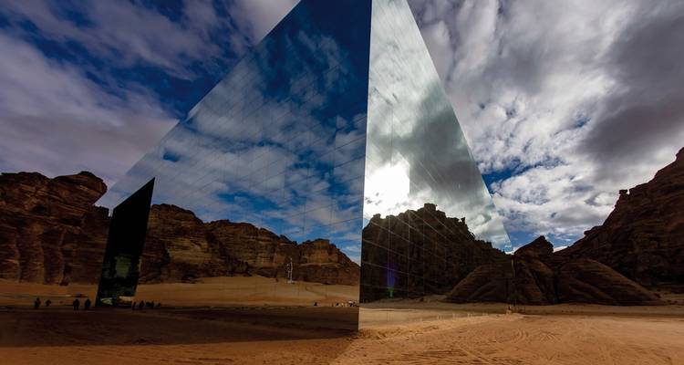 Reflective glass building under a cloudy sky in the desert.