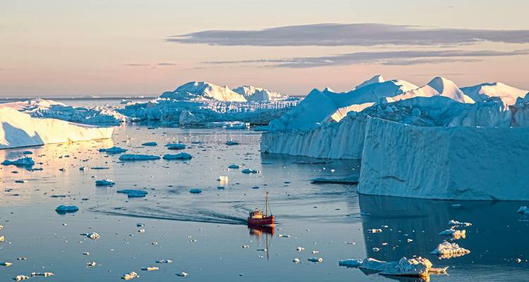 Icebergs in a fjord with a small boat on calm water during sunset.