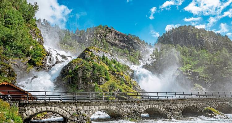 Cascada dramática en una zona montañosa con un puente de piedra.