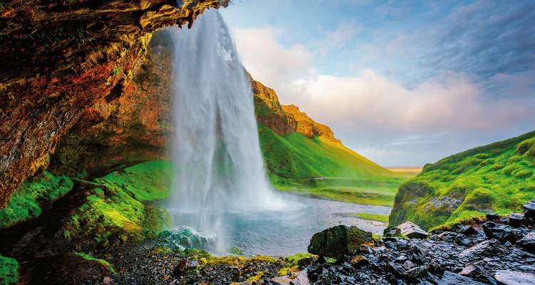 Eine Perspektive von hinter einem Wasserfall mit einem hellen Himmel.