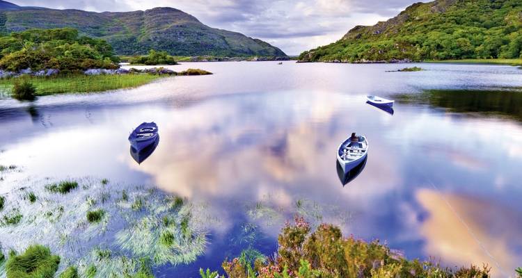 Ruhiger See mit Booten und Bergen im Hintergrund.