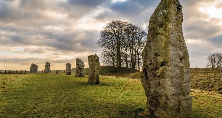Rij van prehistorische monolieten staat op golvend grasland met dramatische door wolken verlichte luchten.