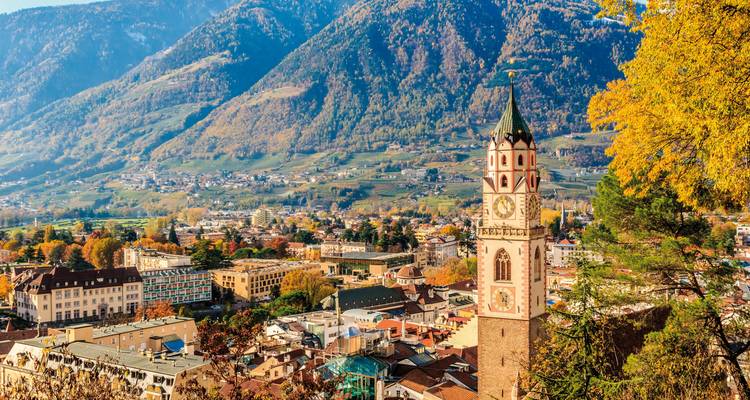 Torre del reloj con montañas en follaje otoñal, Italia.