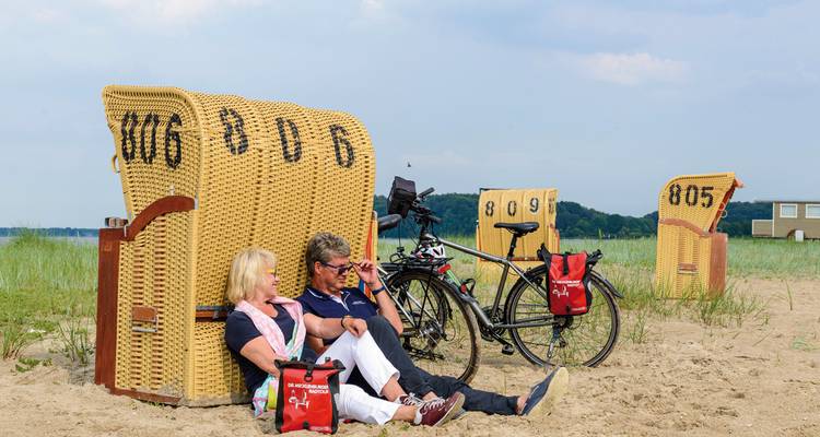 Couple sitting on a beach with bicycles and beach chairs.