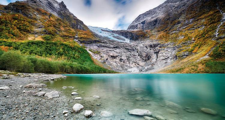 Ein ruhiger See umgeben von Bergen mit einem sichtbaren Gletscher in der Ferne.