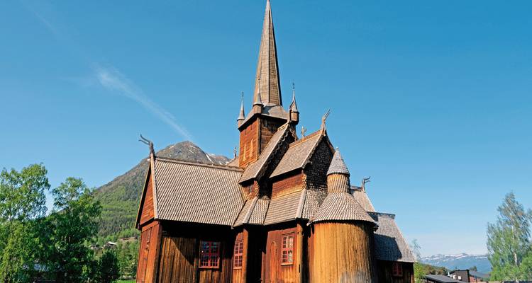 Eine alte hölzerne Stabkirche vor einer Bergkulisse.