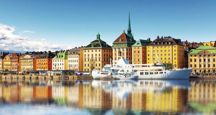Classic Stockholm waterfront with spired church, colorful facades and reflections in calm water.