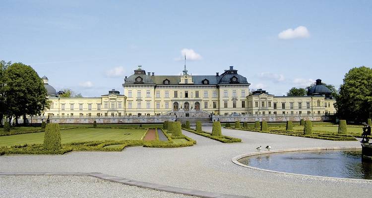 Elegant yellow Drottningholm Palace with manicured gardens and fountain on sunny day.