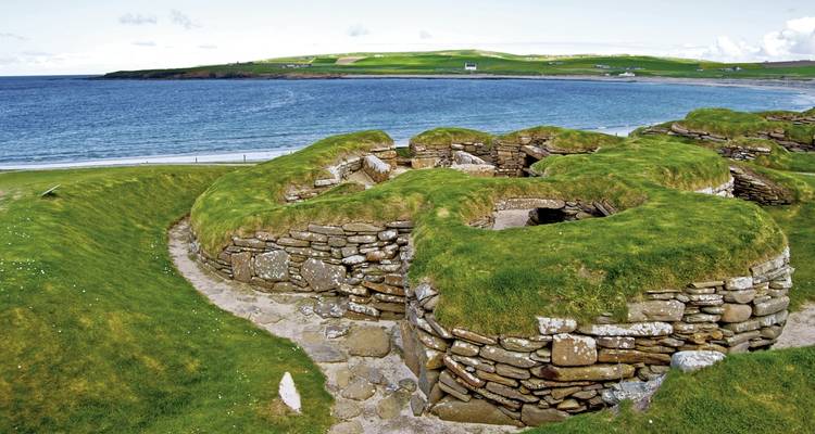 Ancient stone structures with grass rooftops by the sea.