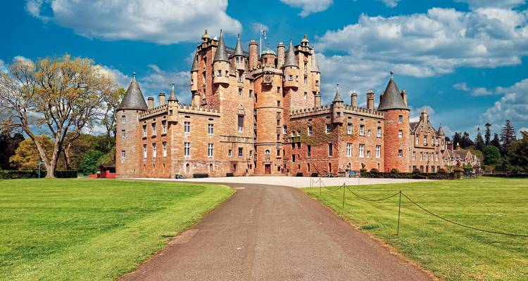 Grand castle with pointed towers, surrounded by green lawns.