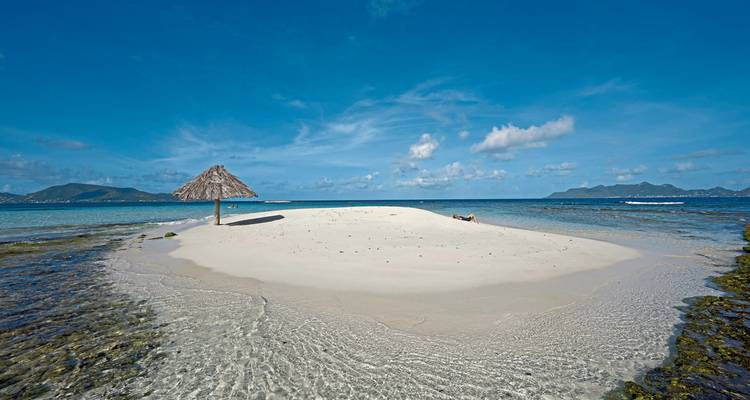 A small sand island with a thatched umbrella and ocean view.