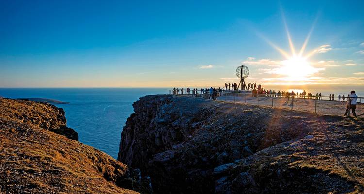 A group of people enjoying the sunset at a viewpoint on a cliff.