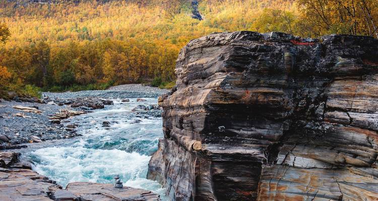 A rocky river with autumn foliage on the banks.