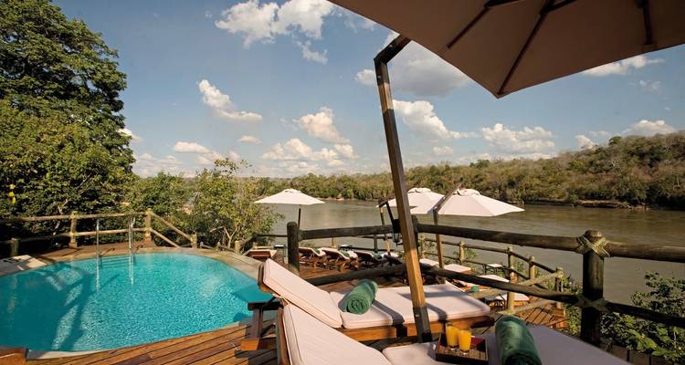 Zone de piscine avec chaises longues et parasols au bord d'une rivière.