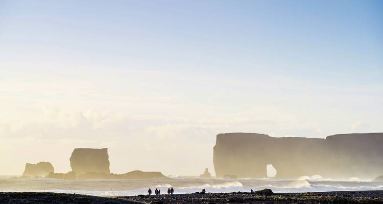 Ruhiger Strand bei Reynisfjara mit entferntem Felsbogen.