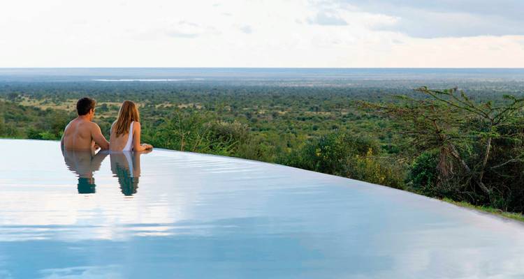 Paar entspannt an einem Infinity-Pool mit Blick auf weite Landschaft
