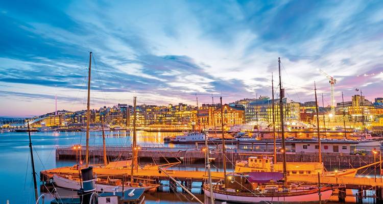 Marina with boats at dusk, cityscape in the background.