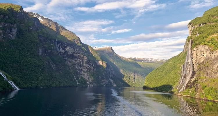 Malerischer Blick auf einen Fjord, umgeben von steilen Bergen und einem Wasserfall.