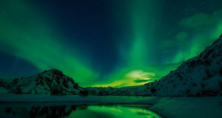 Nordlichter, die sich über eine verschneite, bergige Landschaft spiegeln.