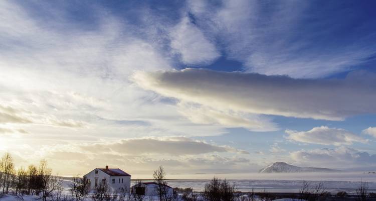 Einsames Haus in einer weiten schneebedeckten Landschaft unter einem blauen Himmel.