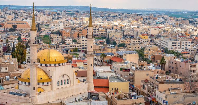 A cityscape featuring a mosque with golden domes and urban skyline.