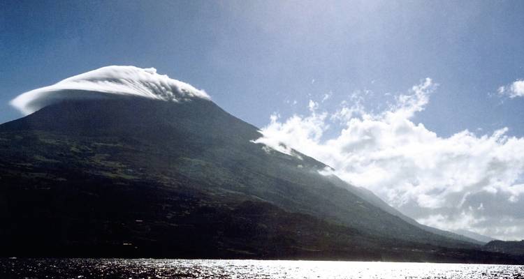 Berg mit einer einzigartigen Wolkenformation über seinem Gipfel, vom Meer aus betrachtet.