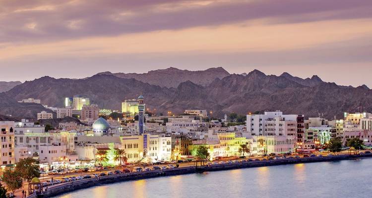 Meerblick auf eine Stadt mit leuchtenden Lichtern, Berge im Hintergrund.